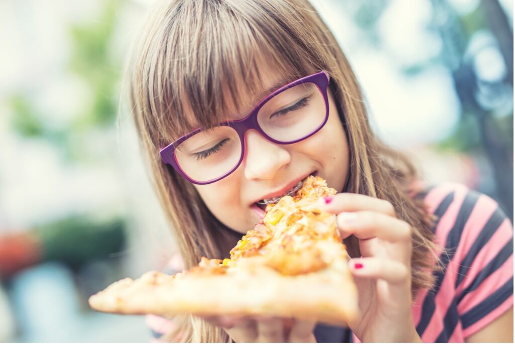 A young person with braces eating a slice of pizza