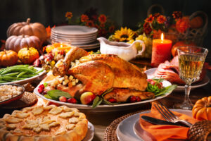 Thanksgiving dinner. Roasted turkey garnished with cranberries on a rustic style table decoraded with pumpkins, vegetables, pie, flowers, and candles, Holiday Braces & Aligners Care: Protect Your Smile During Thanksgiving Feasts