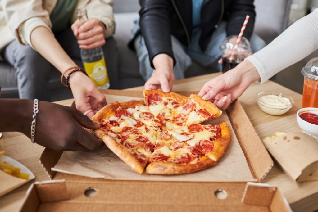 a group of people each grabbing a slice of pizza from a pizza box, Holiday Braces & Aligners Care: Protect Your Smile During Thanksgiving Feasts