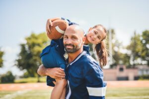 A person holding a child with a football on his shoulders, Children's Orthodontic Care: Celebrating Healthy Smiles This February