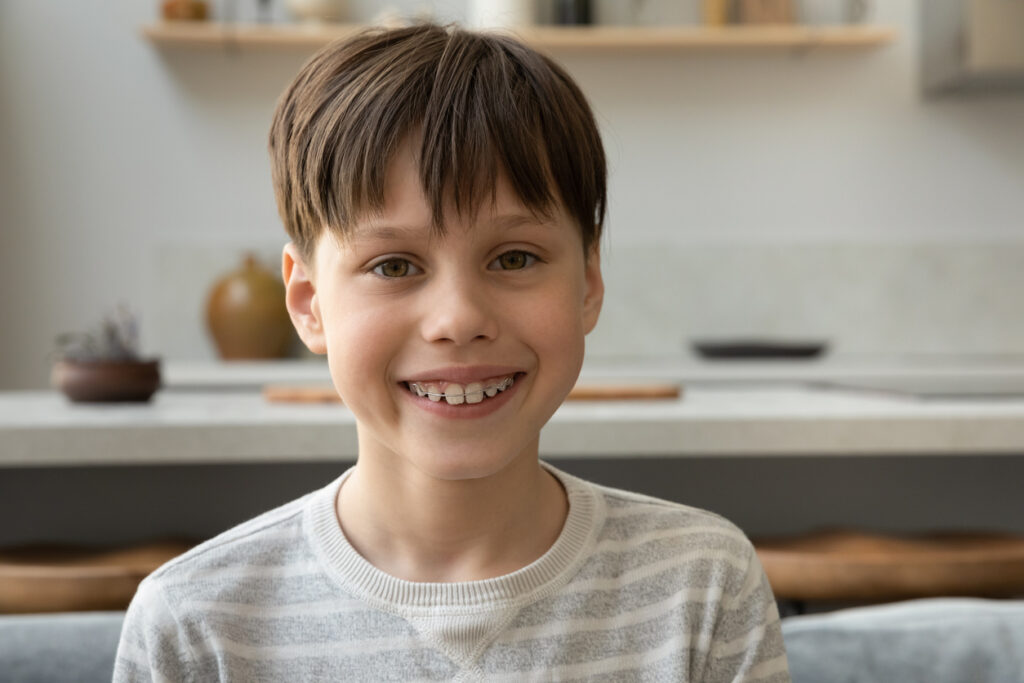 Understanding Orthodontic Timing: When Should Children See an Orthodontist?, Happy early teenage boy with dental metal braces on teeth looking at camera, smiling during online conference chat, video call. Pre teen pupil kid, school student home head shot portrait